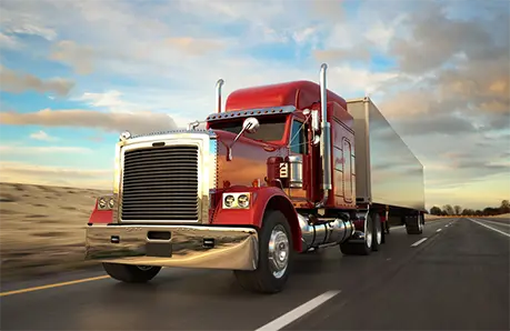 Red semi-truck with a large trailer driving on an open highway under a partly cloudy sky during sunset
